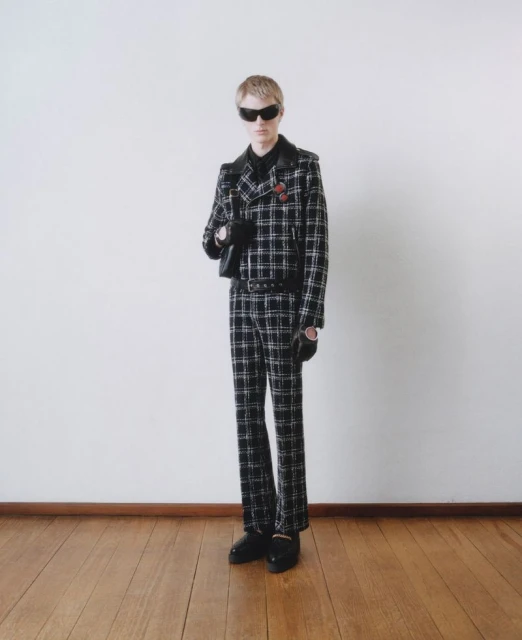 Fashionable young adult posing in a black and white checkered suit with dark sunglasses in a studio setting. Full-length shot, clean background.