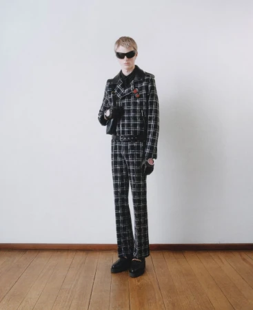 Fashionable young adult posing in a black and white checkered suit with dark sunglasses in a studio setting. Full-length shot, clean background.
