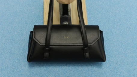 Black leather shoulder bag by Oroton displayed on a wooden stand against a textured blue background