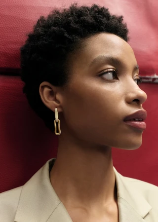 Close-up portrait of a woman wearing sculptural earrings and a beige jacket against a red background for Somersault project.