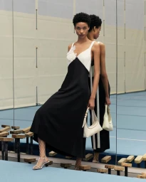 Model in black and white dress with floral detail holding a white handbag standing near a mirror