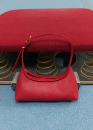 A red leather shoulder bag resting in front of a red upholstered cushion and exposed springs.