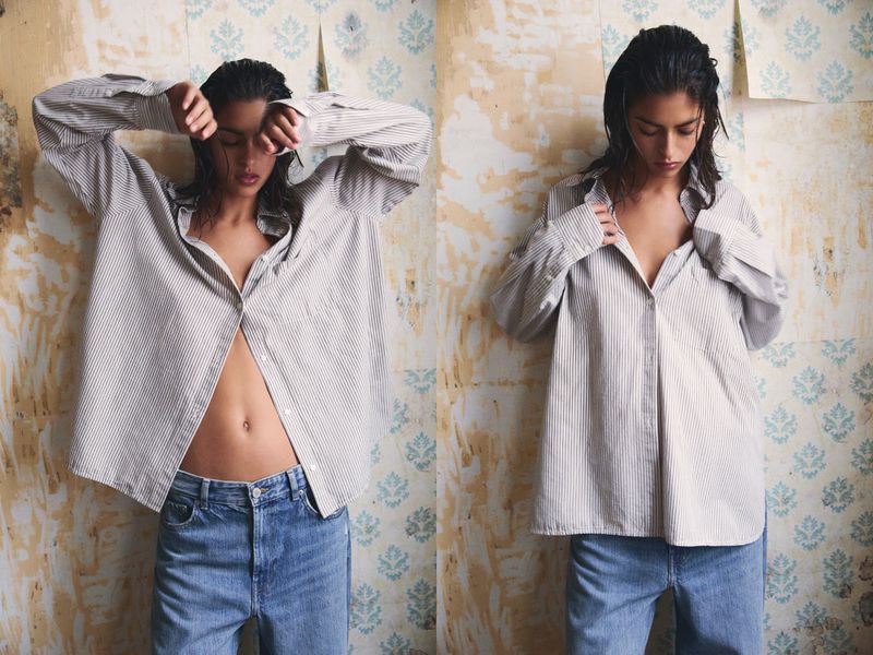 A young adult woman poses in a striped shirt and blue jeans against a patterned wall, creating a casual fashion editorial look indoors.