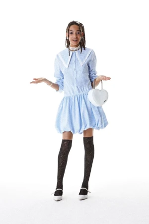 Full-shot of a young adult woman wearing a light blue polka-dot dress and black patterned stockings, holding a heart-shaped white purse.
