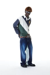Model wearing blue denim jeans, colour-blocked polo shirt, fur hat, and white sunglasses against white background