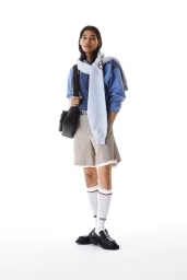 Model wearing a blue patterned jacket, draped grey sweatshirt, beige tailored shorts, and white knee socks against a white studio background.