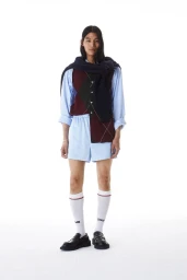 Model Kyosuke Akiyoshi poses in an argyle knit vest, light blue shorts, white tube socks, and black chunky loafers on a white backdrop.