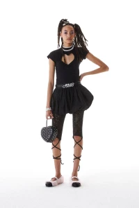 Model in black heart-cutout top and bubble skirt holding a heart handbag against a white background