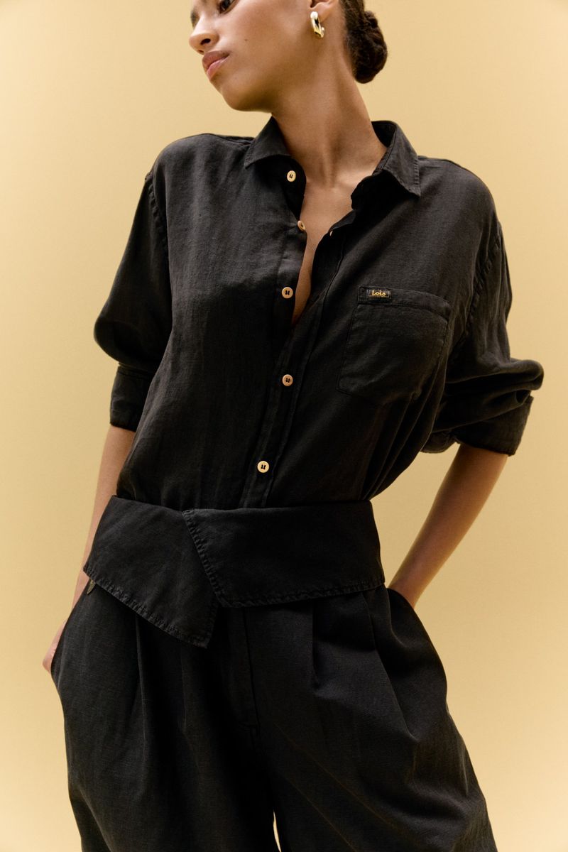 Elegant portrait of an African-American woman in a black linen shirt and pants, styled with a high waist and set against a pale yellow backdrop.