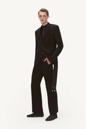 A male model poses in a black blazer, shirt, and pants outfit in a studio, exuding sleek fashion in a full-length, eye-level shot.