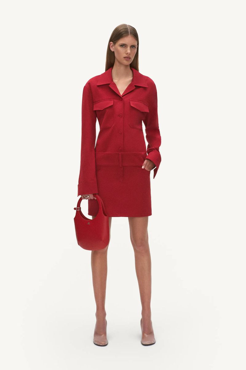 A slender woman poses in a red collared dress and blush-toned heels, holding a matching red handbag against a neutral background.