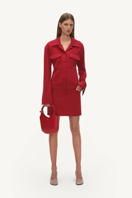 A slender woman poses in a red collared dress and blush-toned heels, holding a matching red handbag against a neutral background.