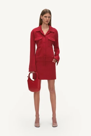 A slender woman poses in a red collared dress and blush-toned heels, holding a matching red handbag against a neutral background.