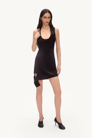 A slender fashion model poses in a fitted black mini dress and black high heels against a white backdrop in a studio setting.