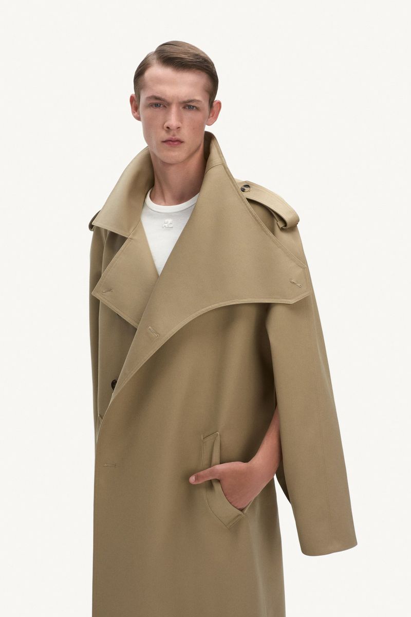 Male model posing in a tan trench coat against a white background in a fashion forward studio shot. Fashion and style concept.