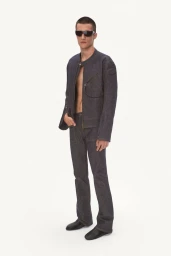 Model wearing a dark raw denim jacket, matching straight-leg trousers, and black sunglasses against a white studio background.