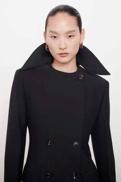 Headshot of a stylish Asian woman wearing a black double-breasted blazer with a large collar and earrings against a white backdrop.