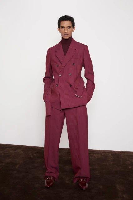 Fashionable man poses in a double-breasted maroon pinstripe suit with matching turtle neck and brown leather loafers against a white backdrop.