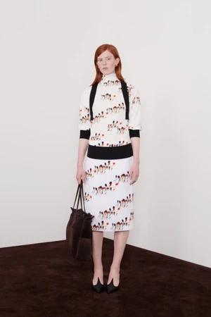 Model Laura Rudd in a floral print top, matching skirt, and black trim holding a brown tote bag for Ferragamo Resort 2025.
