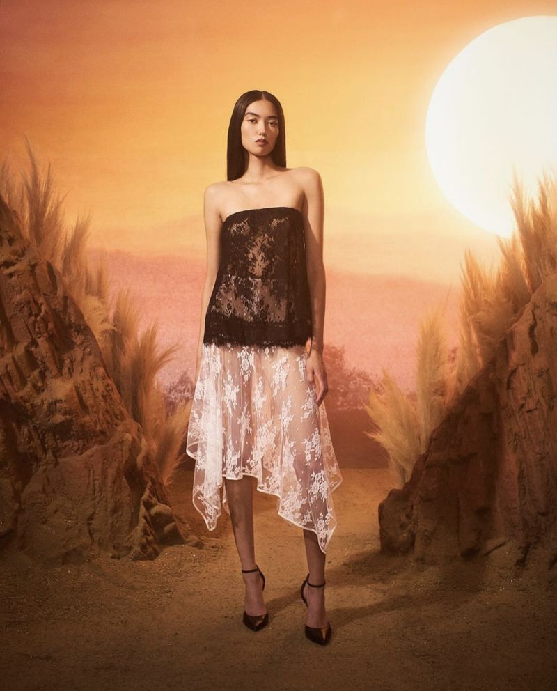Elegant Asian woman in strapless black lace top and white lace skirt standing in outdoor setting with golden hour lighting. Fashion shot.