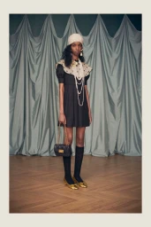 Model Amina Hassan in a black dress with a polka dot collar, layered pearl necklaces, and gold shoes for Valentino Resort 2025.