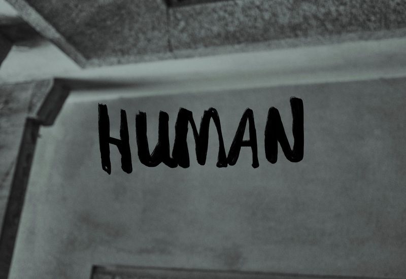 Black and white abstract image of the word HUMAN written on a wall with a monochromatic color scheme and a textured surface.