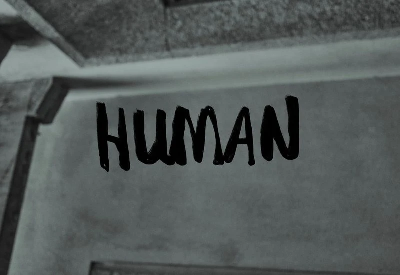 Black and white abstract image of the word HUMAN written on a wall with a monochromatic color scheme and a textured surface.