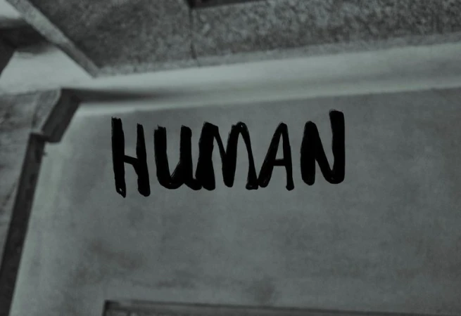Black and white abstract image of the word HUMAN written on a wall with a monochromatic color scheme and a textured surface.