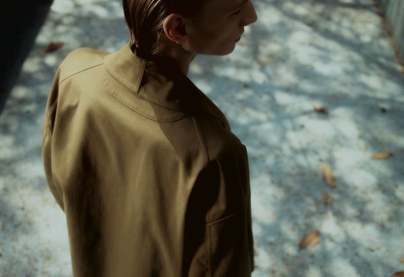 Back view of a young adult male wearing an earth-toned jacket, captured outdoors with natural light and soft shadows, emphasizing fashion.