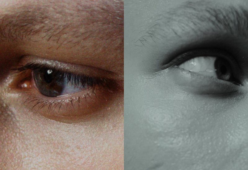 Macro shot showing two human eyes, one in color with brown iris, the other eye in grayscale, side-by-side, close-up of human face.