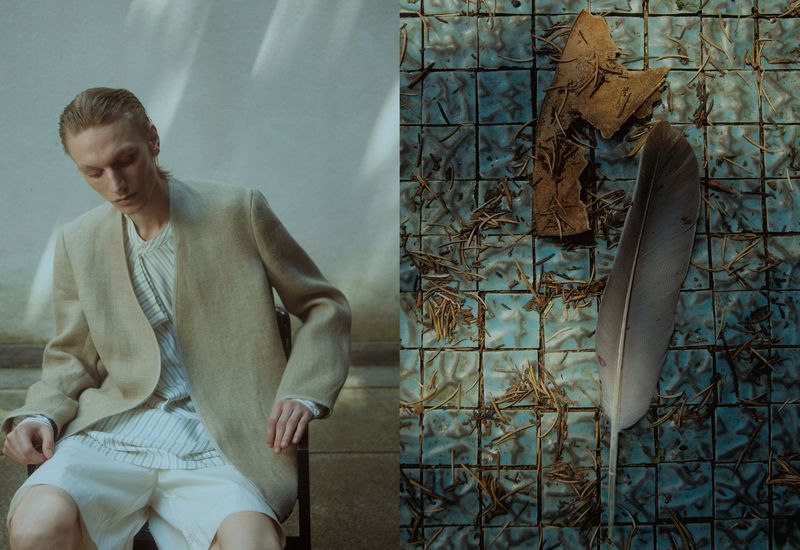 A fair-skinned male model in a beige jacket is seated indoors with a tile background featuring a leaf and a feather.