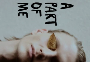 Close-up portrait of a model with a dry leaf covering one eye against a light textured background