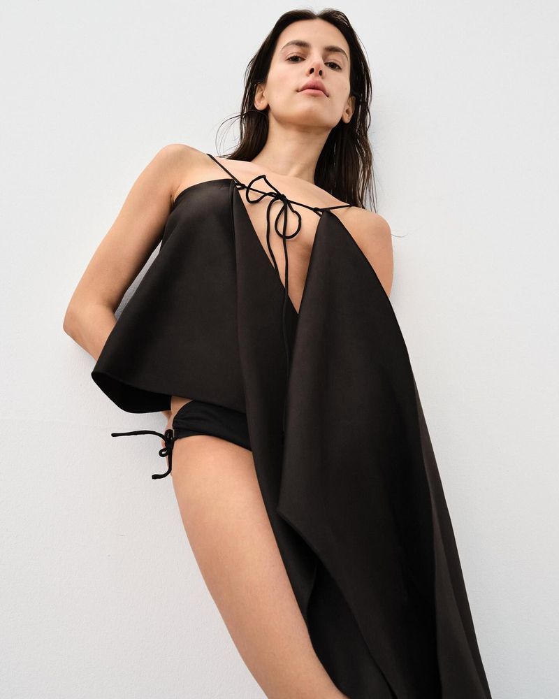 Woman poses in black dress against a white background. Fashion photography showcasing a modern, minimalist style. Studio shot. 
