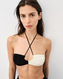 Model Maria Tomaszewska wearing a black and white halter bikini top against a pale grey studio wall background