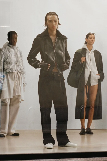 Three fashion models showcase clothing on a white background, including leather jackets, hoodies, long coats, loose pants, and white shoes.