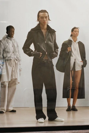 Three fashion models showcase clothing on a white background, including leather jackets, hoodies, long coats, loose pants, and white shoes.