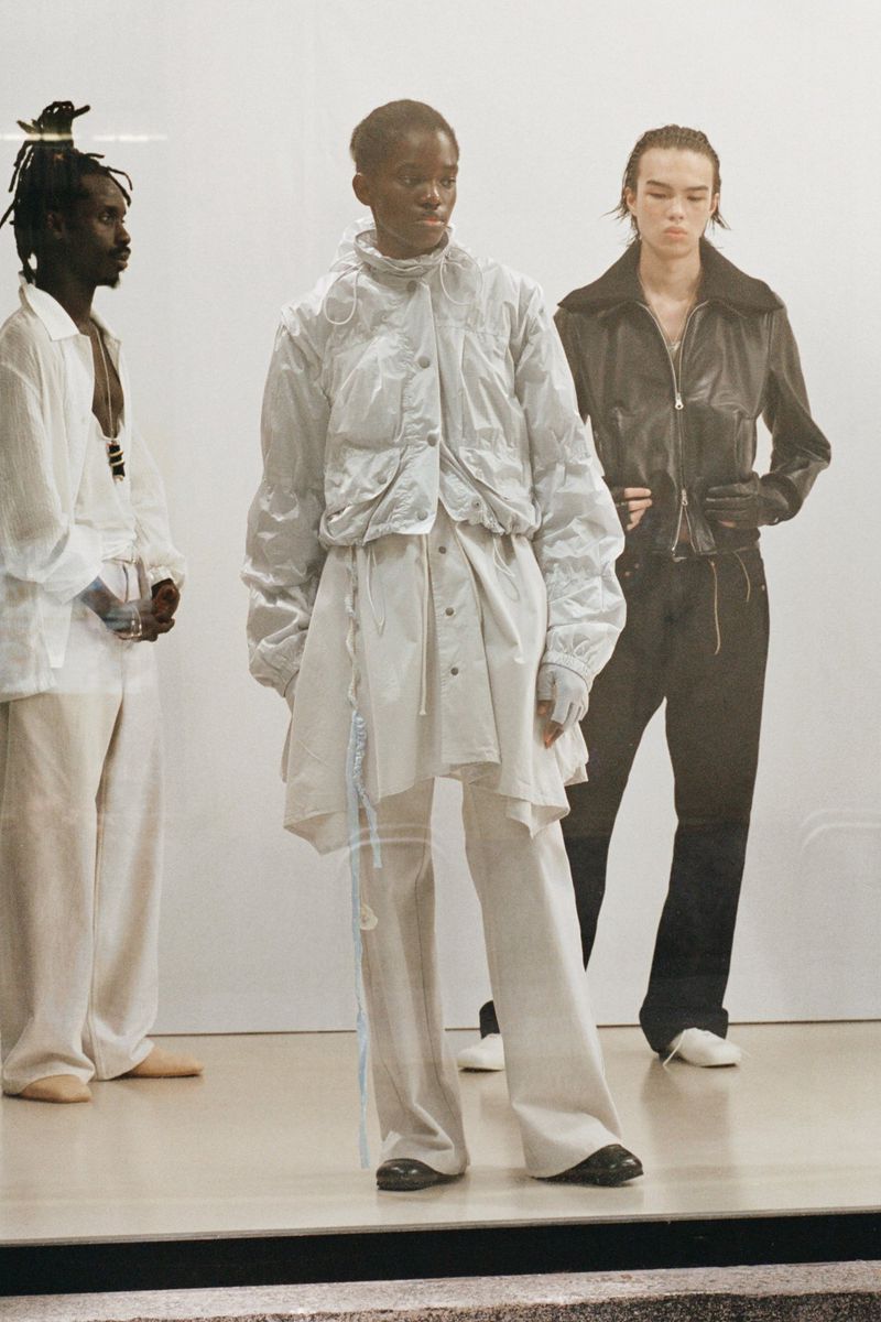 Three fashion models showcase modern, layered clothing in a studio setting with natural light. The focus is on contemporary style and textures.