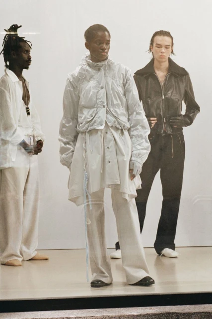 Three fashion models showcase modern, layered clothing in a studio setting with natural light. The focus is on contemporary style and textures.