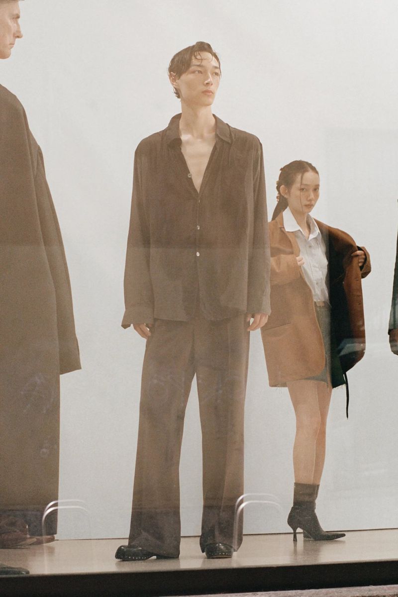 Model in brown button shirt and matching trousers standing in front of a white seamless background