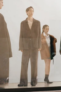 Model in brown button shirt and matching trousers standing in front of a white seamless background
