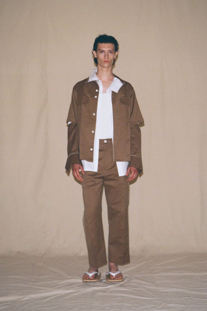 Male model in a brown suit and flip flops stands in a photo studio with a neutral background. Fashion shot with natural lighting.