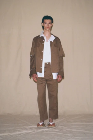 Male model in a brown suit and flip flops stands in a photo studio with a neutral background. Fashion shot with natural lighting.