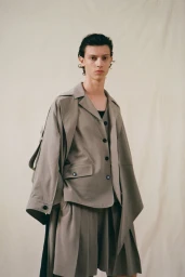 Male model wearing a structured grey jacket and matching shorts against a plain off-white studio backdrop.