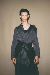 Model Luigi Bianco in a patterned grey shirt and black leather skirt for Setchu spring summer 2025 lookbook.