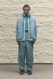 Model wearing a light blue jacket and matching trousers standing against a textured off-white wall for A-Cold-Wall