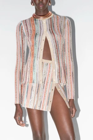Fashion shot of a Black female model in a patterned knit skirt suit with gold collar necklace, posing in front of a white backdrop.