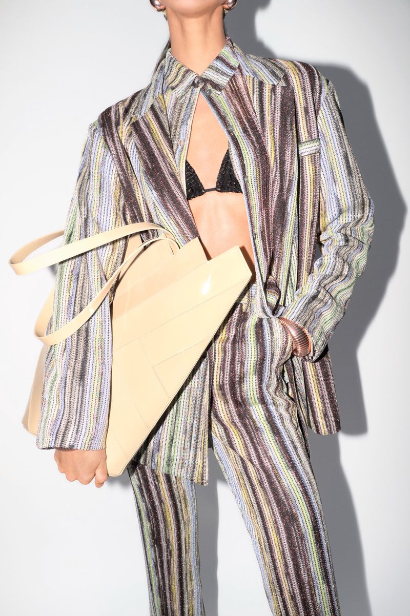 Woman in a striped suit and triangle purse. The model is wearing a black bikini top underneath the open blazer. The background is a white wall.