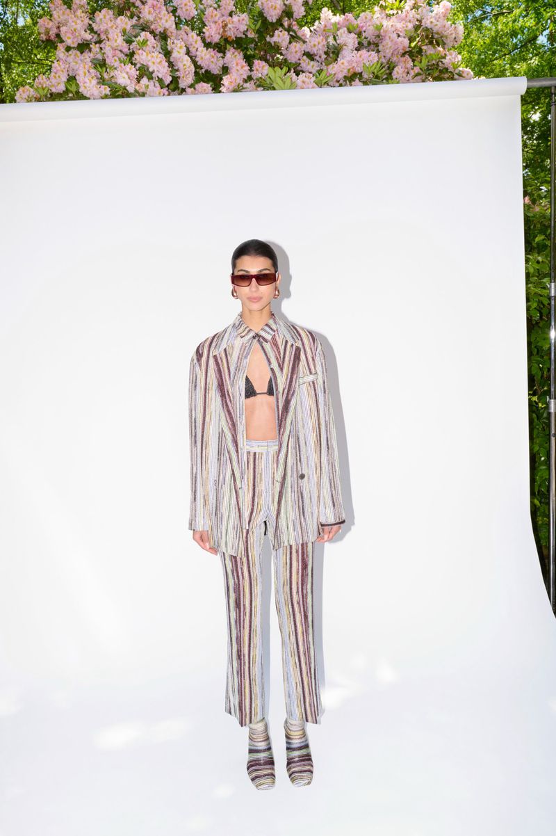 Woman in a striped suit poses against a white backdrop with cherry blossoms. She's wearing sunglasses and a black bikini top.