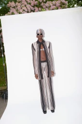 Model in patterned knit cardigan and trousers wearing sunglasses and headscarf against a white backdrop