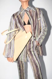 Model wearing a striped suit and black bralette holding a cream tote bag against a white backdrop